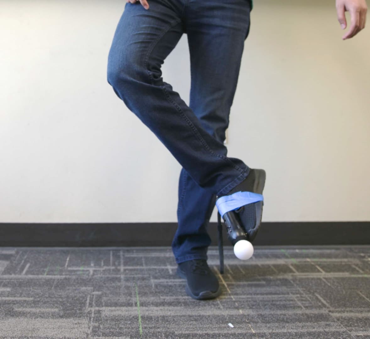 A foot wearing a shoe with a PlayStation Move motion controller taped to it. The leg is being swung to the user's left.