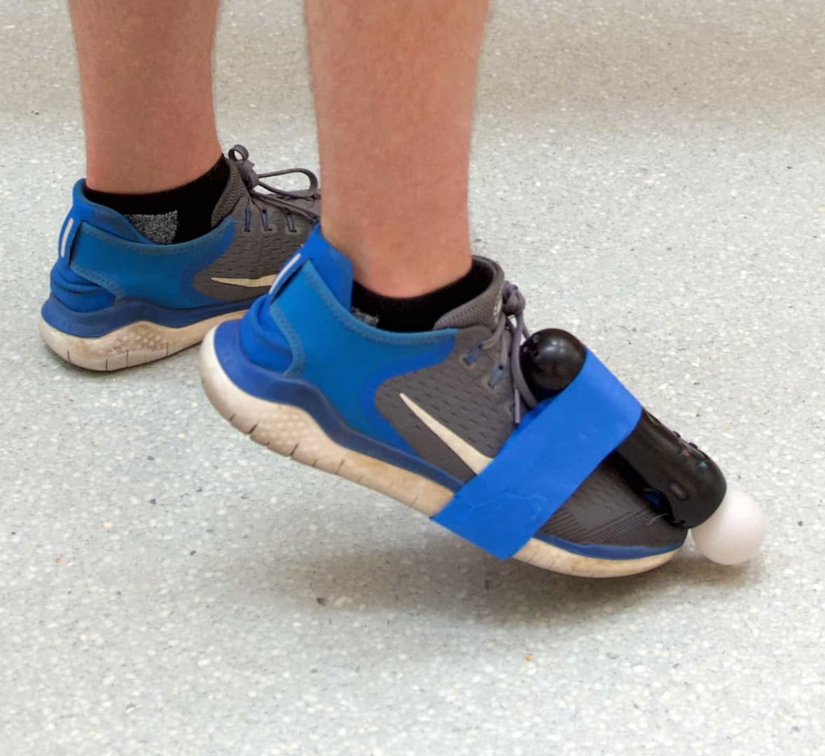 A foot wearing a shoe with a PlayStation Move motion controller taped to it. The foot is being pointed downwards towards the floor.