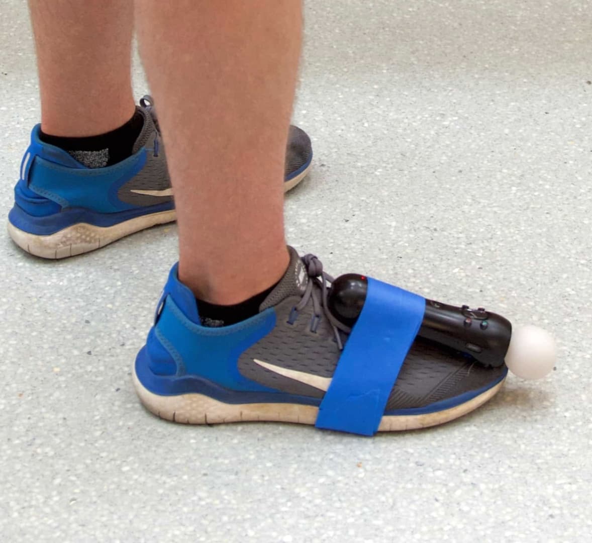 A foot wearing a shoe with a PlayStation Move motion controller taped to it. The foot is flat on the floor.