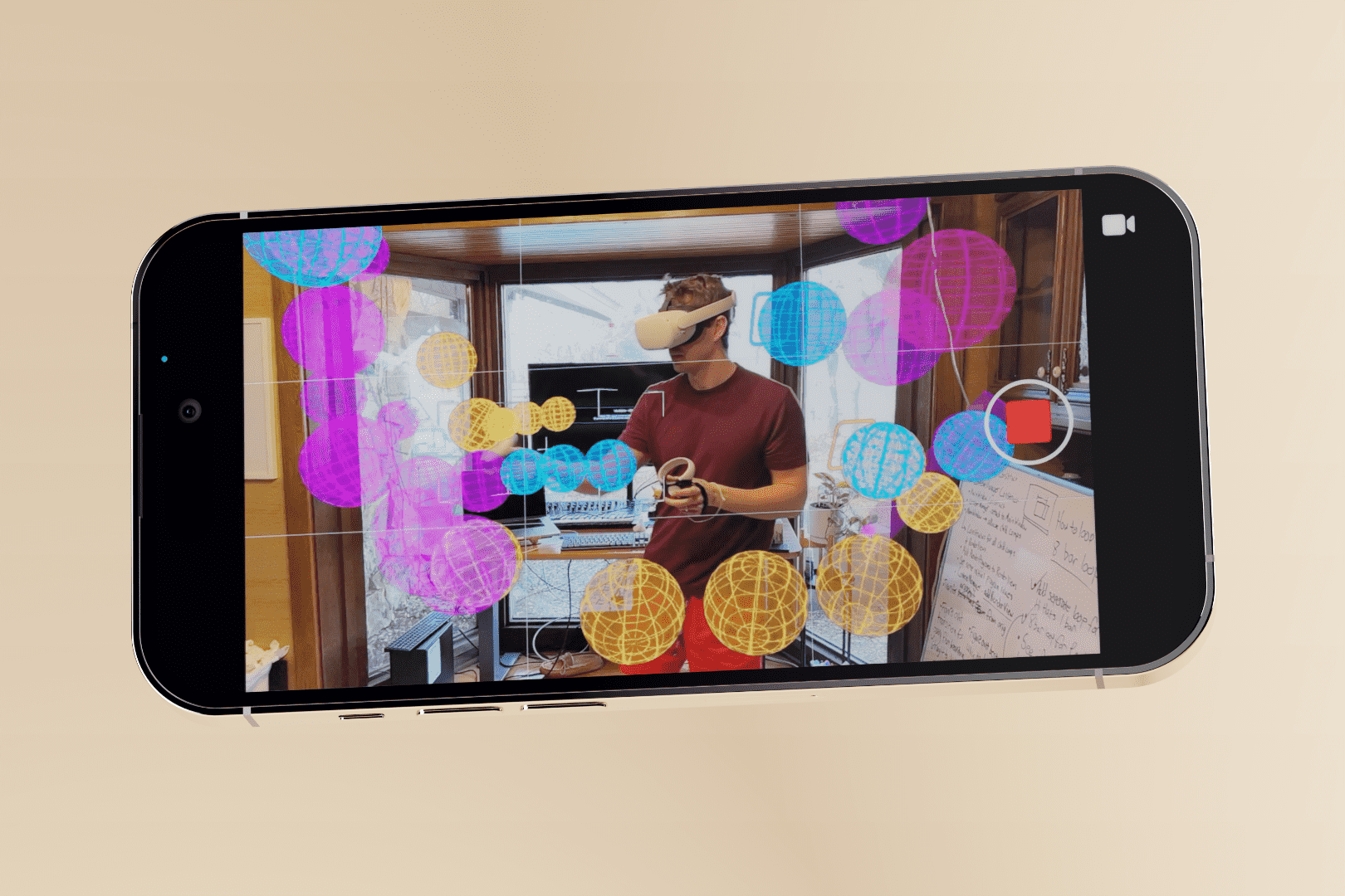 An iPhone shows the UI of a video recording app that is recording a man wearing a VR headset surrounded by translucent virtual spheres.